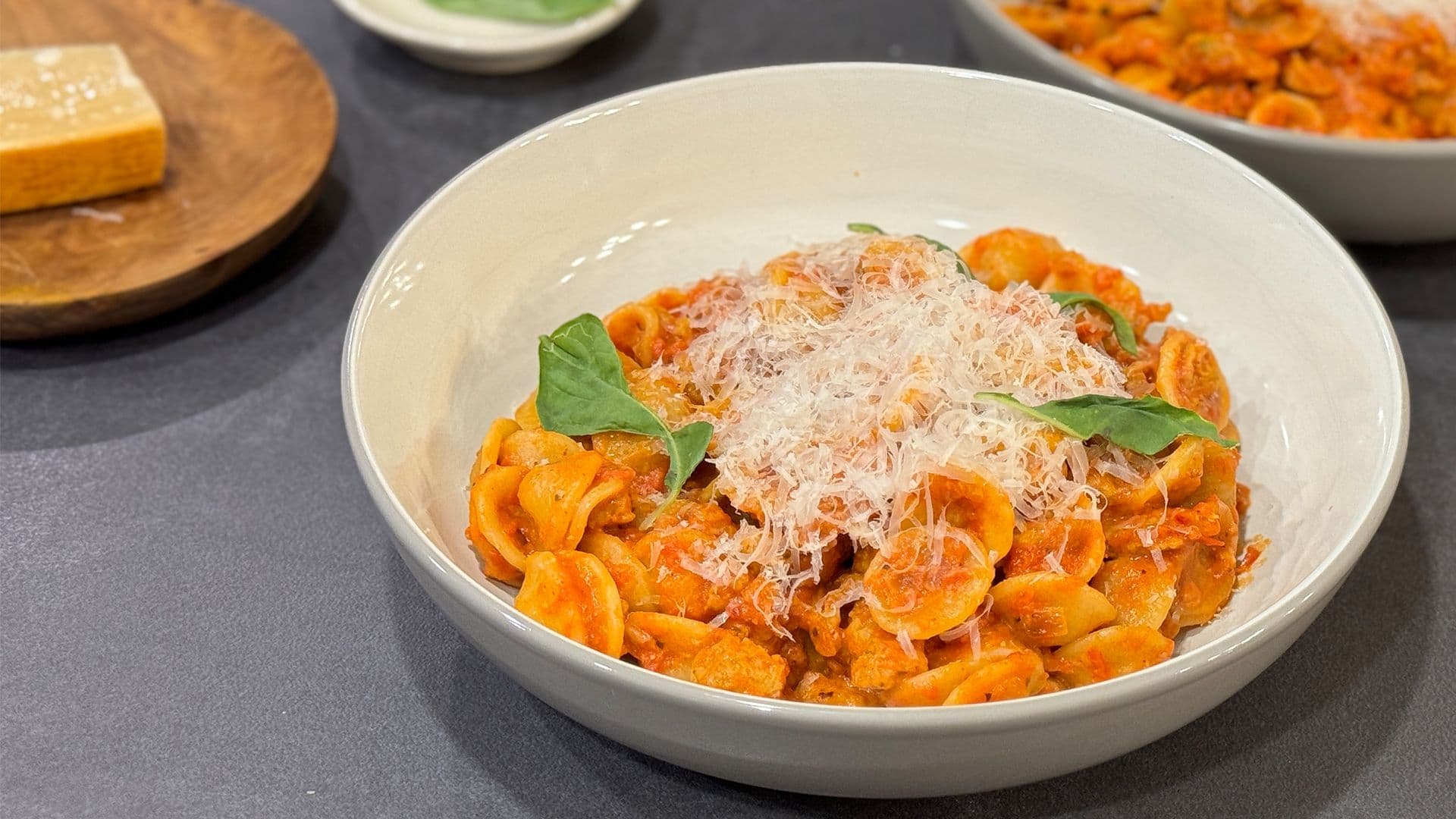 Orecchiette pasta with spicy Italian chicken sausage topped with grated Parmesan cheese and fresh basil in a white bowl.