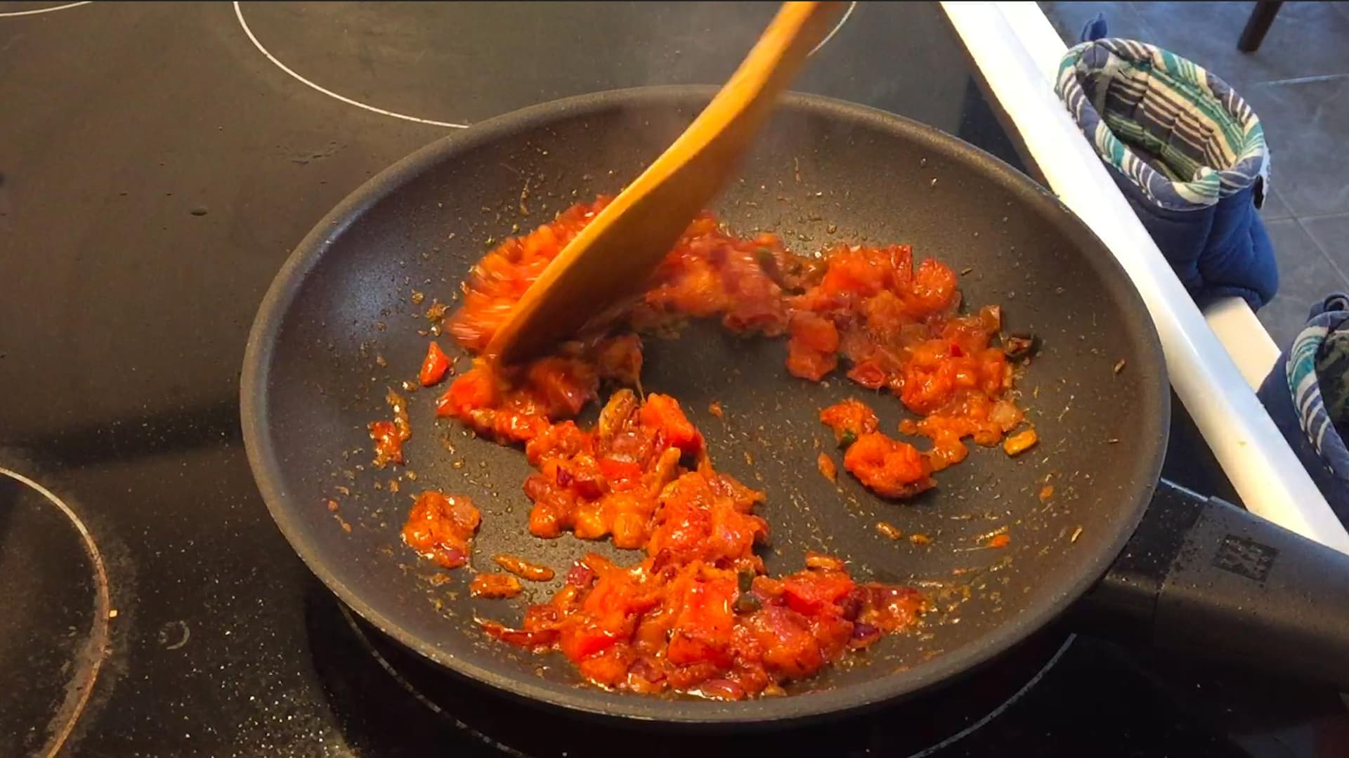 Diced tomatoes and red chilies cooking in a pan with a wooden spoon during tadka preparation for chana dal.