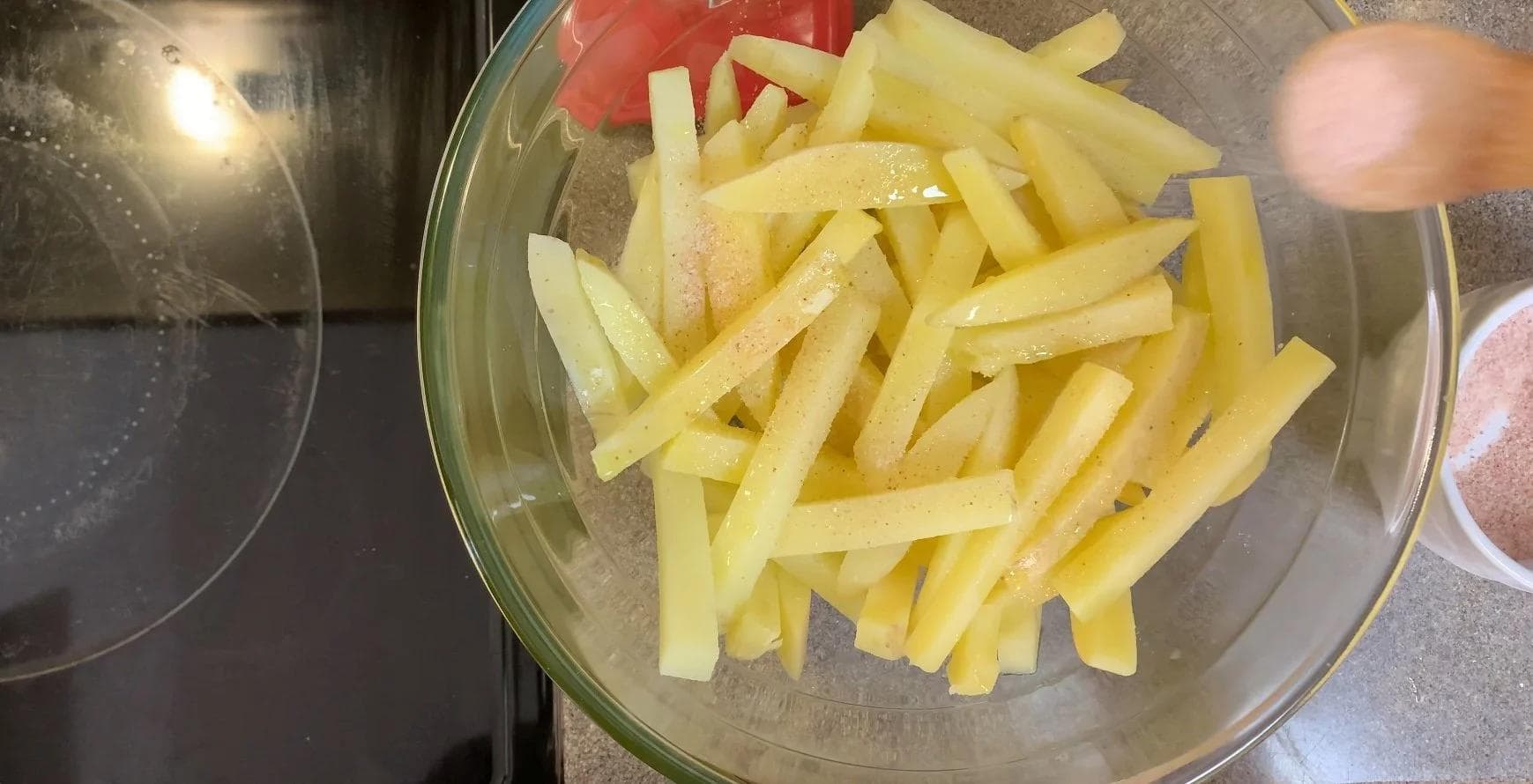 Seasoned french fries tossed with salt and olive oil in a glass bowl, ready for baking.