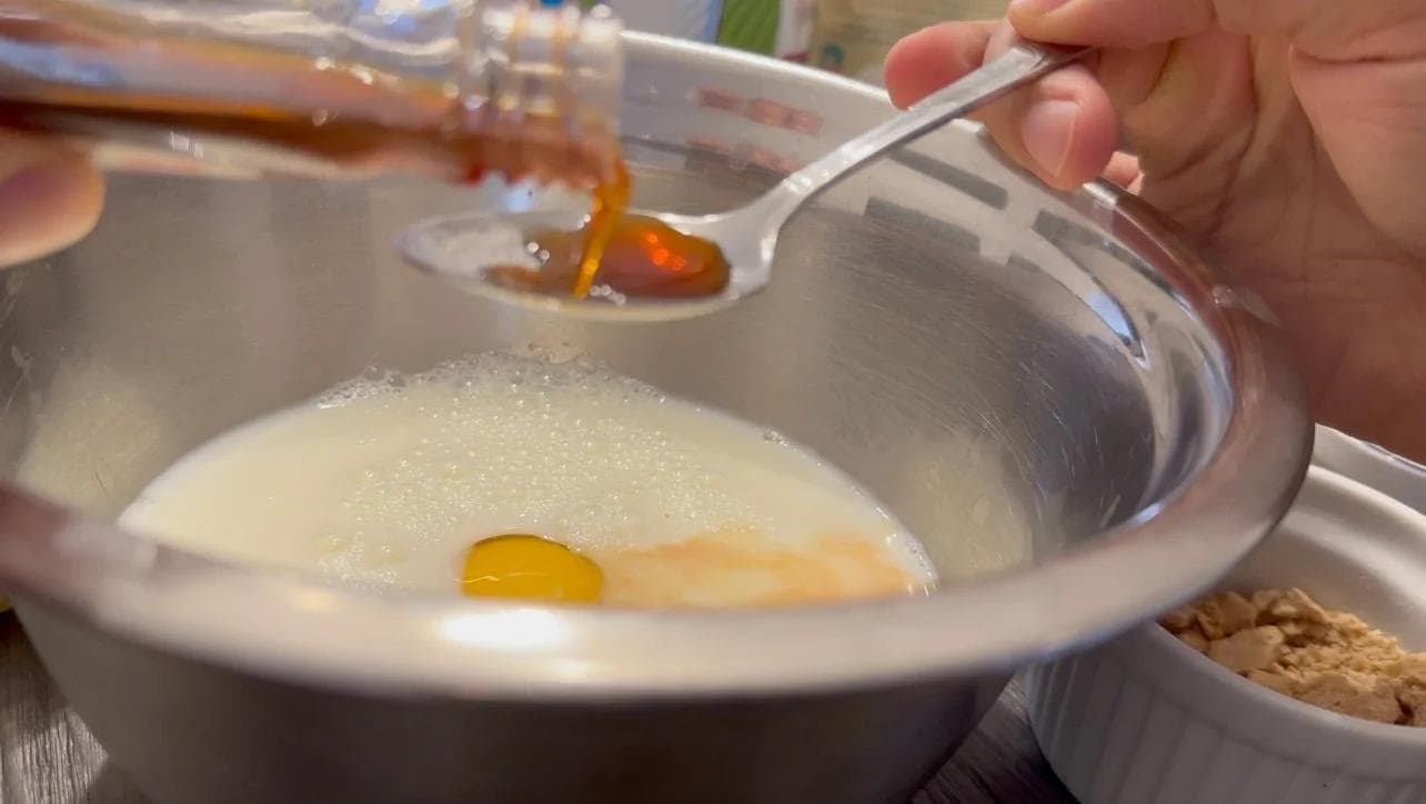 Pouring wet ingredients into a bowl of dry ingredients for s'mores pancake batter with graham crackers visible.