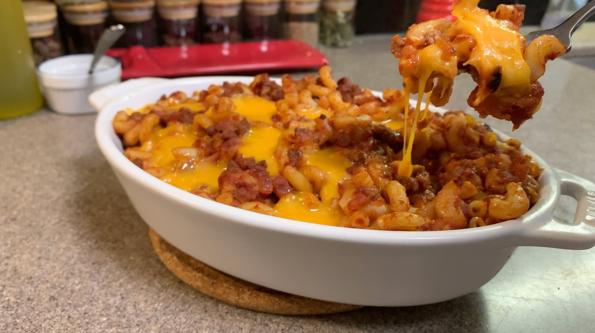 Baked cheeseburger mac and cheese being lifted from white casserole dish with melted cheddar cheese and ground beef visible.