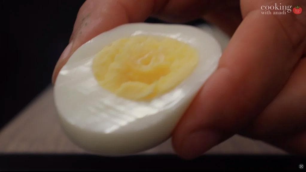 Halved hard-boiled egg showing white and creamy avocado-filled yolk mixture being held in hand.