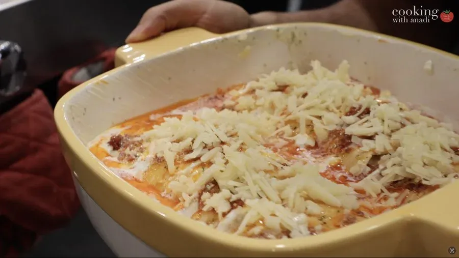 Gluten-free strukli in a cream-colored baking dish topped with melted cheddar cheese before baking.
