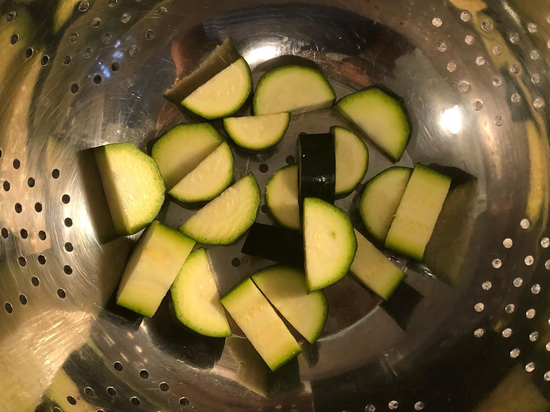 Diced zucchini pieces in a metal colander, prepared for salting in a Mediterranean pasta recipe.