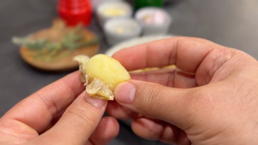 Hand holding a peeled baby potato with skin partially removed over a cooking workspace
