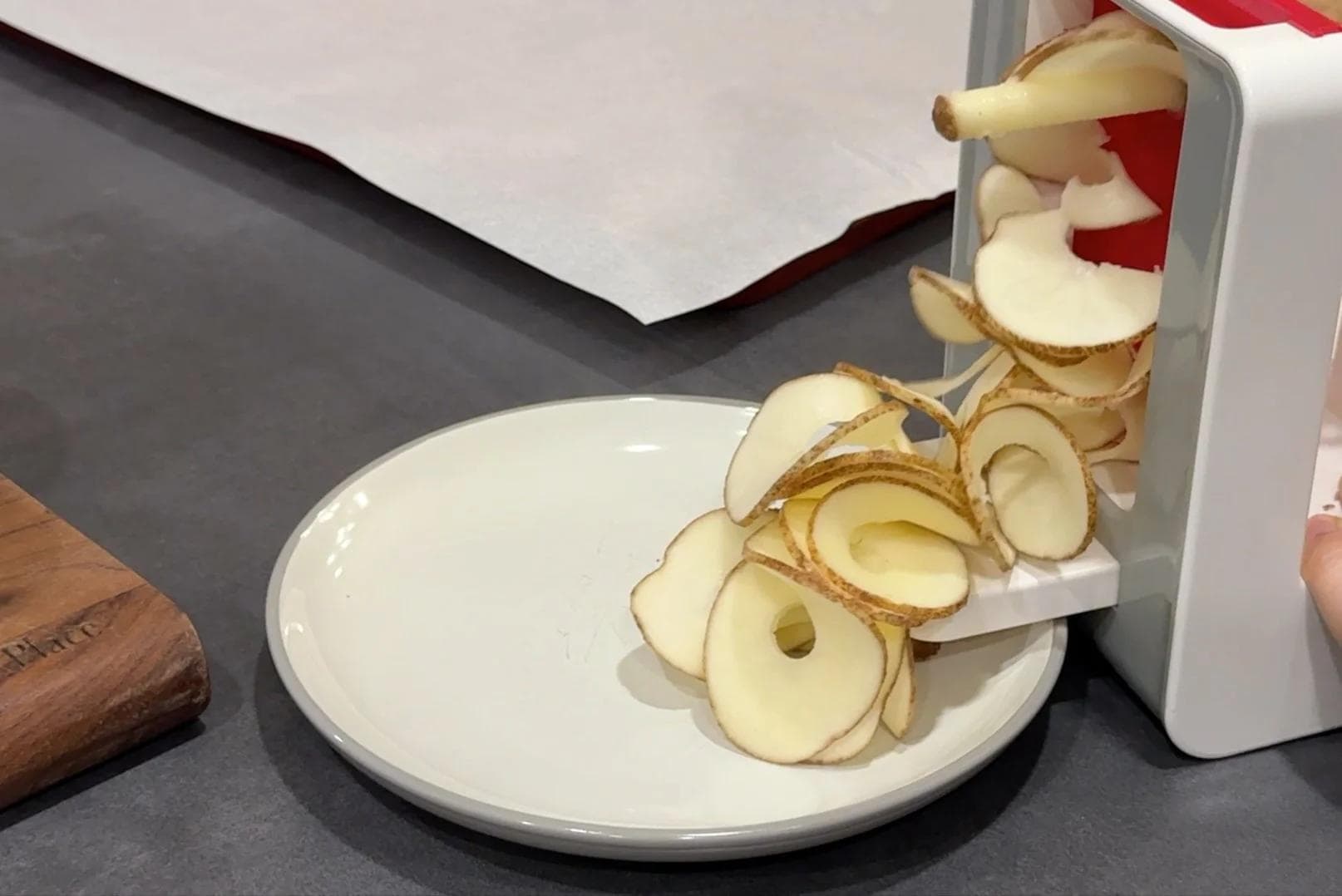 Thinly sliced potatoes spiralized and arranged on a white plate next to a white kitchen tool.