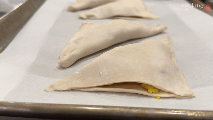 Potato-filled puff pastry triangles sealed with fork marks on parchment paper, ready for air frying.