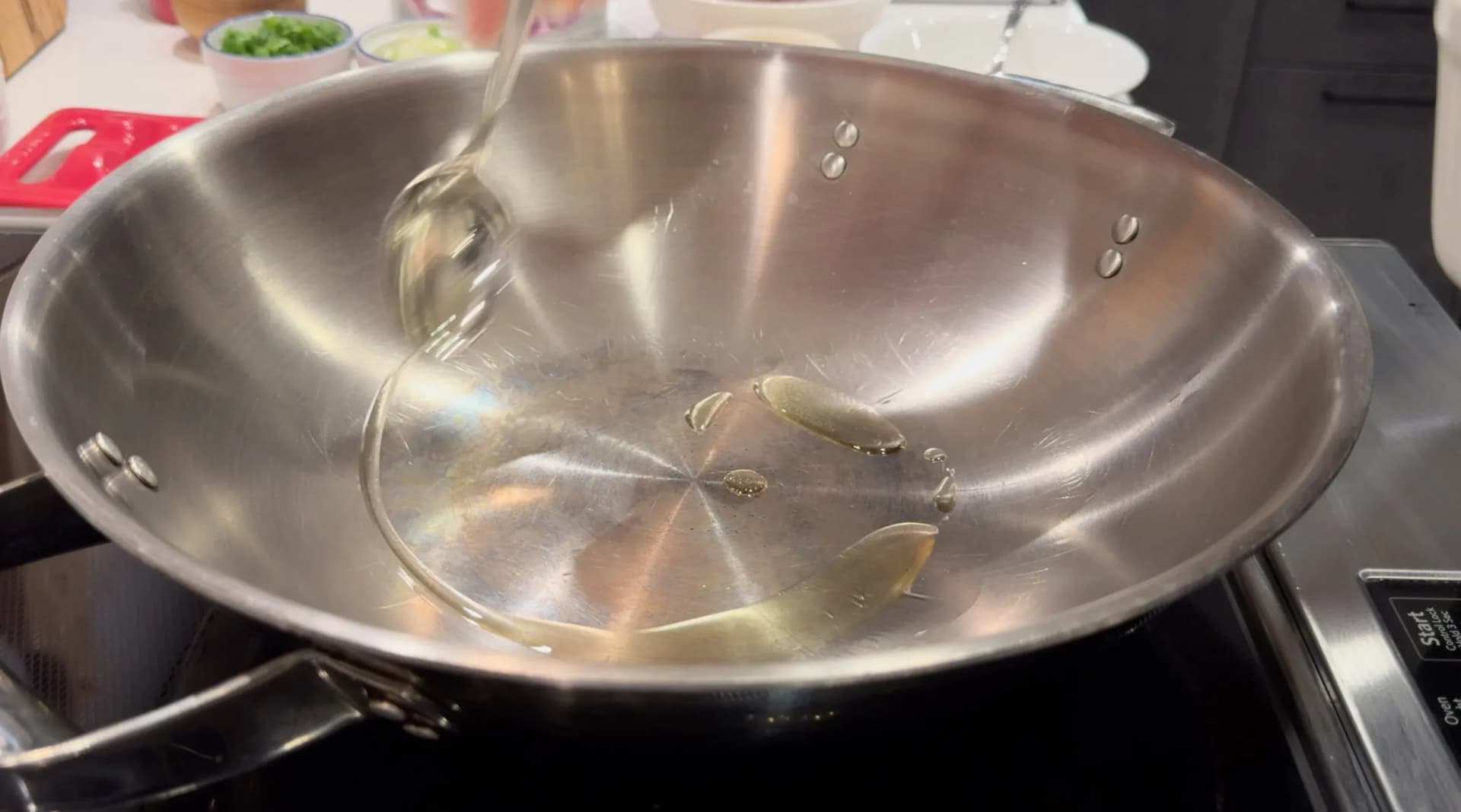 Oil and bay leaves heating in a stainless steel wok on an induction cooktop, with a ladle resting inside.