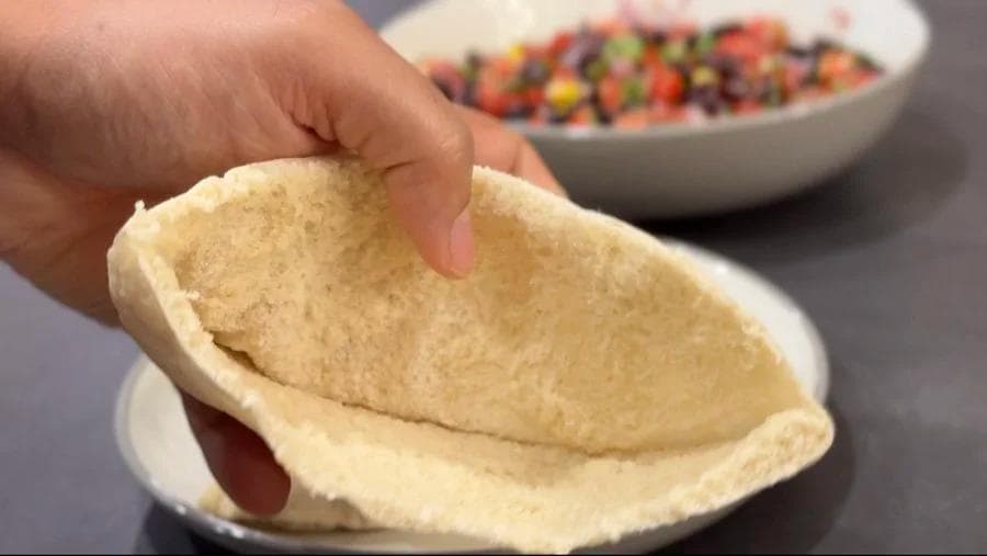 Hand holding open a warm pita pocket ready to be filled with vegan black bean and corn mixture.