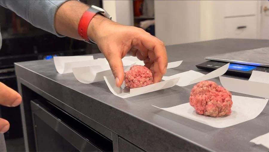 Hand placing seasoned ground beef patty on parchment paper next to another formed burger patty.