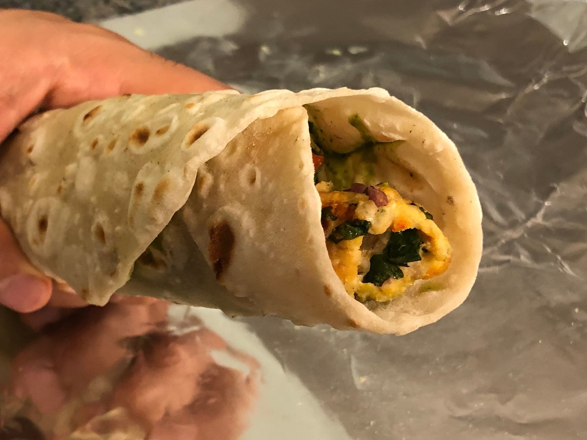 Chicken seekh kebab roll wrapped in paratha with cilantro-mint chutney, onions, and tomatoes, held in hand.