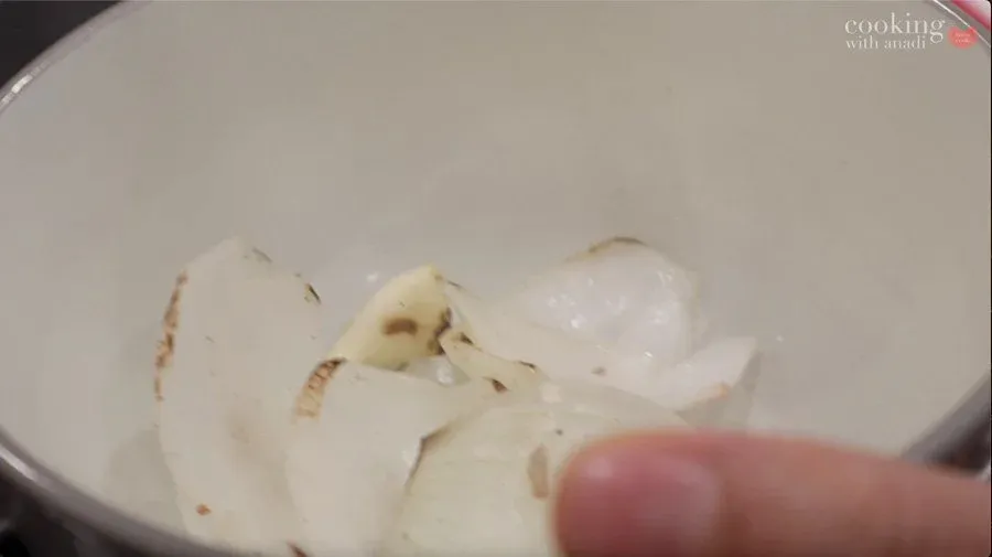 Charred onion and garlic cloves in a white pan during salsa roja preparation.
