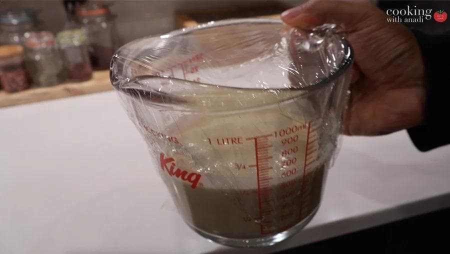 Crepe batter in a measuring cup covered with plastic wrap, chilled before cooking.
