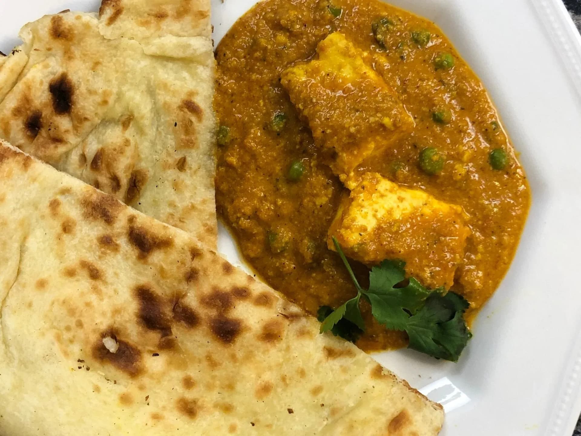 Matar paneer curry served with roti on a white plate, garnished with green peas and cilantro.