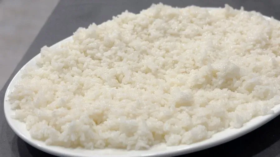 Cooked sushi rice in white grains piled on an oval white plate, fluffy and separated.