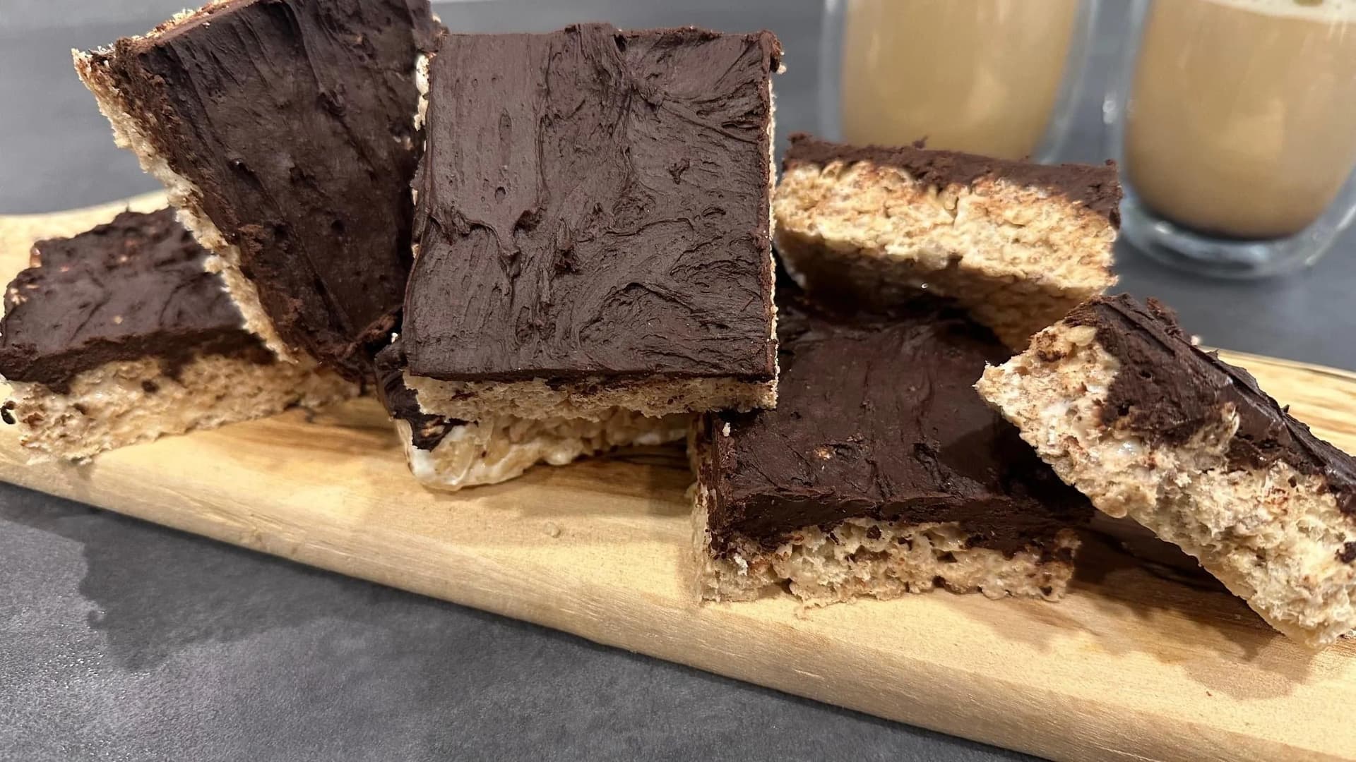 Protein Rice Krispies treats with chocolate frosting on a wooden board, served with milk.