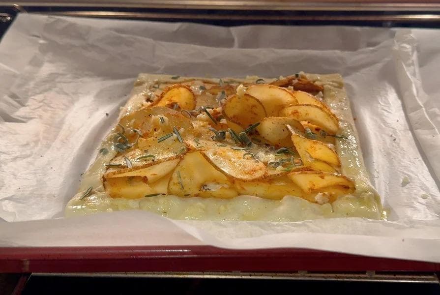 Golden baked puff pastry tart topped with sliced potatoes, rosemary, and garlic butter on parchment paper.
