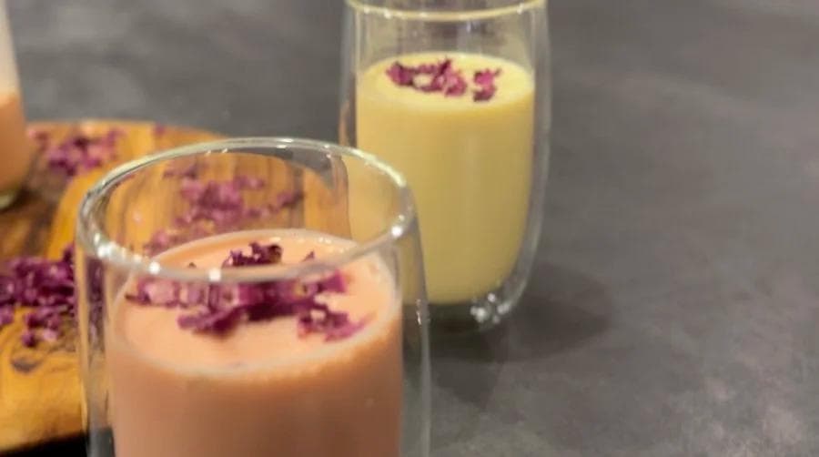 Two glasses of Gulabi Doodh with creamy pink and pale yellow layers, garnished with dried rose petals.