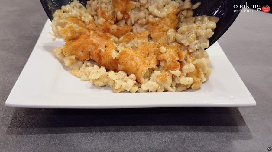 Käsespätzle with golden crispy crust plated on white plate, topped with caramelized onions and pepper.