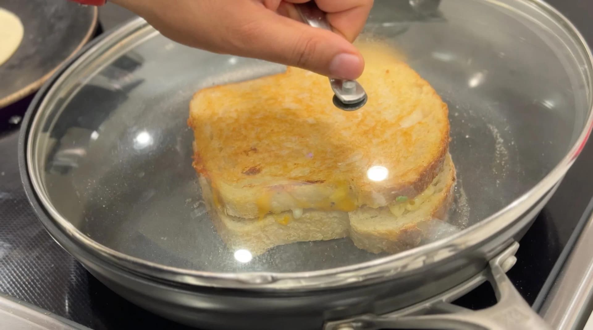 Golden-brown grilled cheese sandwich being flipped in a skillet with melted butter.