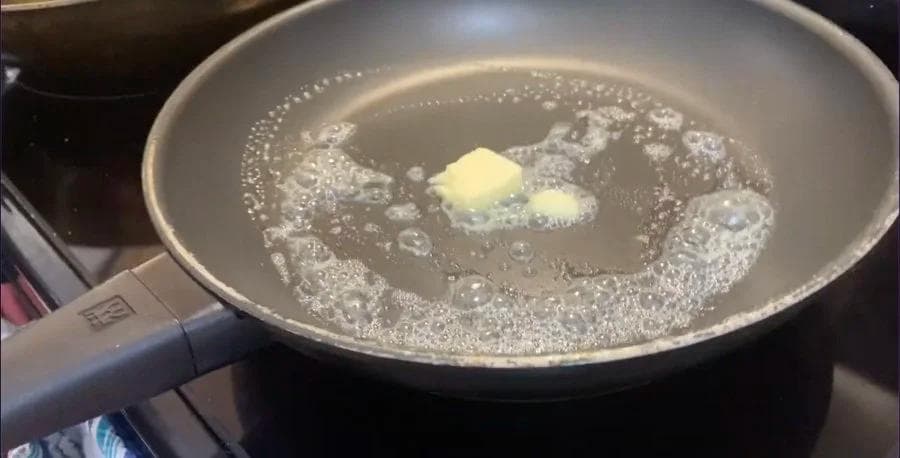 Butter melting in a non-stick pan with cracked eggs ready to be cooked for the breakfast wrap.