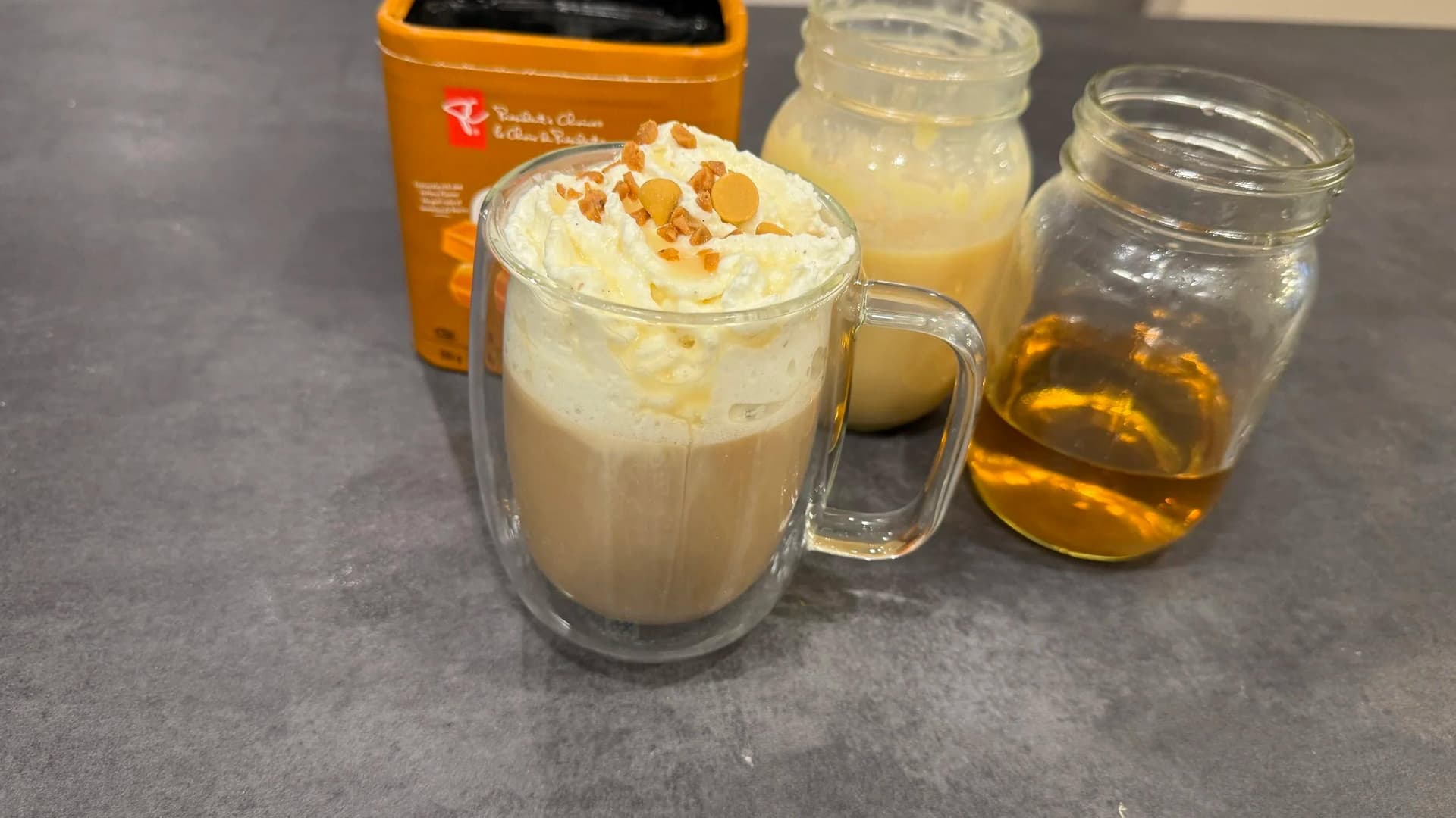 Homemade caramel brulee latte topped with whipped cream and caramel bits in a glass mug, served with ingredients.