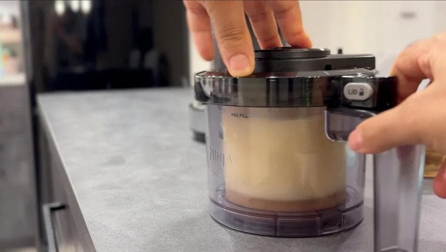 Hands placing a frozen pint container into a Ninja Creami machine for processing.