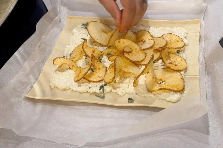 Puff pastry tart topped with ricotta base and sliced potatoes arranged in rows, ready for baking.