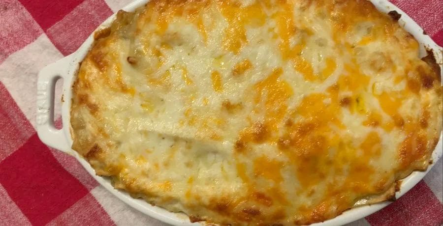 Golden-brown baked white chicken lasagna in a white casserole dish with melted cheese on top.