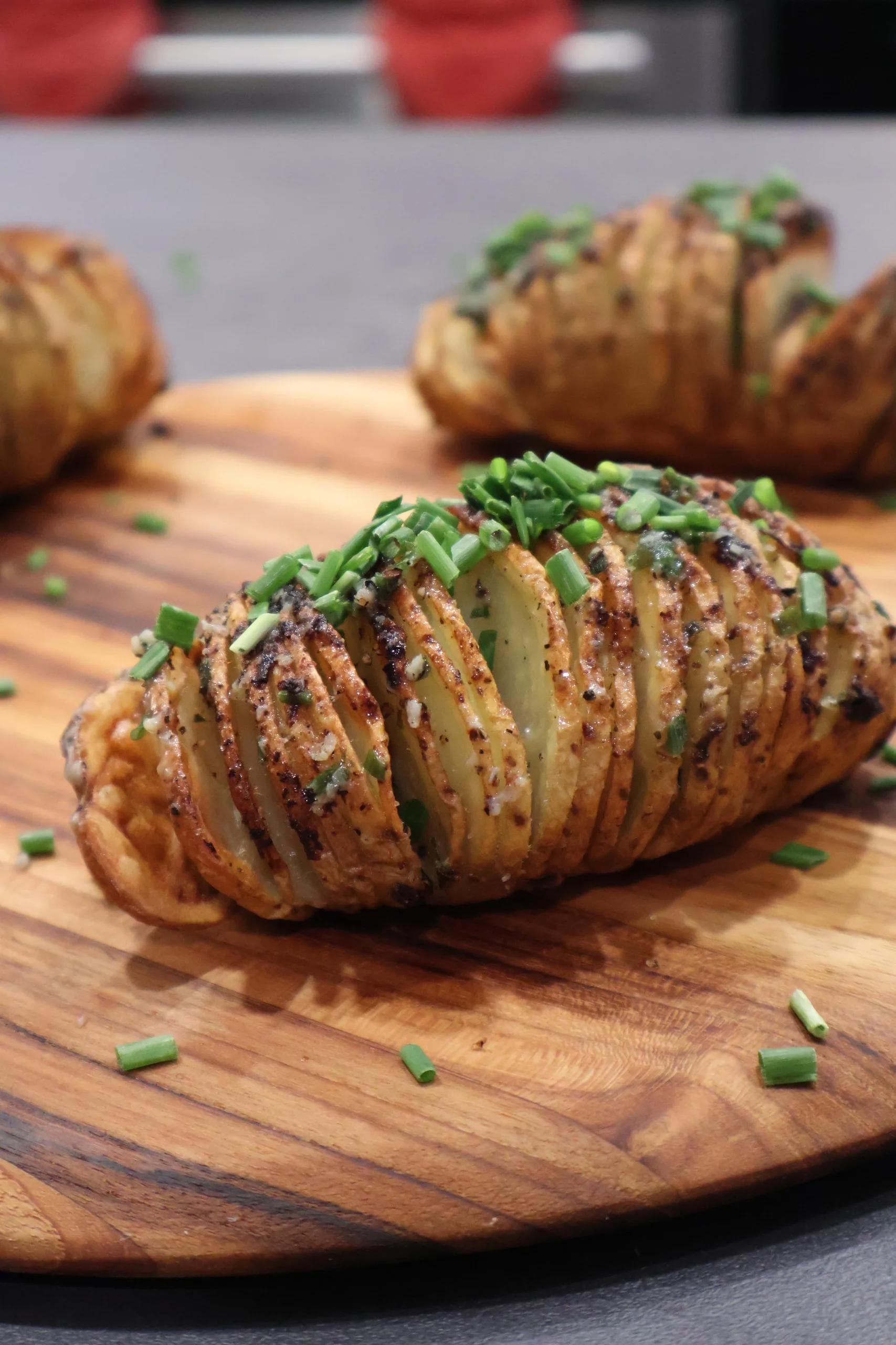 Hasselback potatoes on a wooden board, sliced and topped with melted butter, seasoning, and fresh chopped chives.
