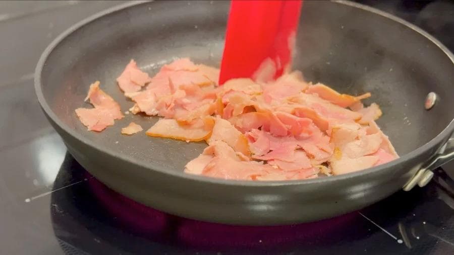 Diced ham cooking in a nonstick skillet with a red spatula, lightly browned and fragrant.