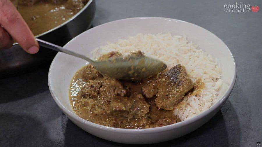 Balinese beef rendang served in a white bowl with white rice, being ladled with sauce.
