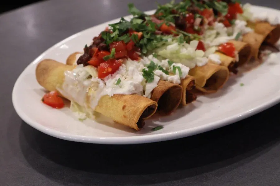 Crispy air fryer taquitos on a white oval plate, topped with sour cream, pico de gallo, shredded lettuce, and fresh cilantro.