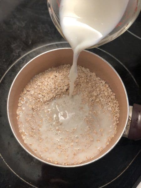 Milk being poured into a pot of dry oats to begin cooking oatmeal.