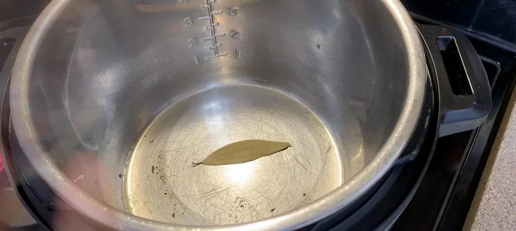 Instant Pot with melted ghee and a bay leaf floating in the center of the inner pot.