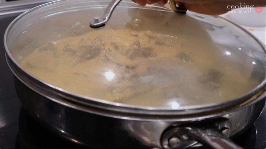 Beef rendang simmering in coconut milk broth with lid on stovetop pot