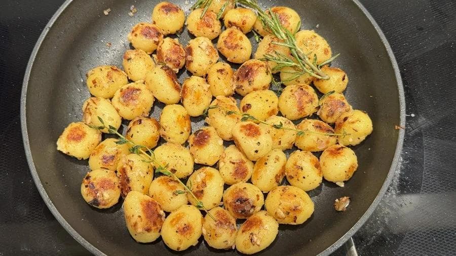 Golden sautéed baby potatoes with fresh rosemary sprigs in a dark skillet, browned and seasoned.