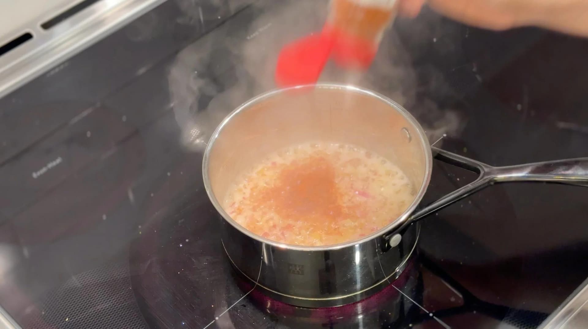 Creamy cheese sauce simmering in a saucepan on stovetop during preparation of scalloped potatoes.