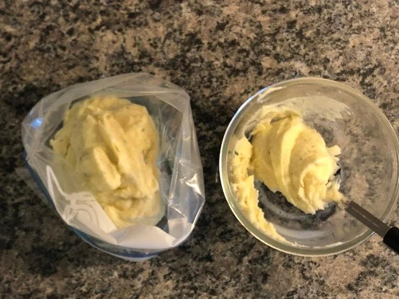 Mashed potatoes in a ziploc bag and glass bowl, prepared for piping onto shepherd's pie.