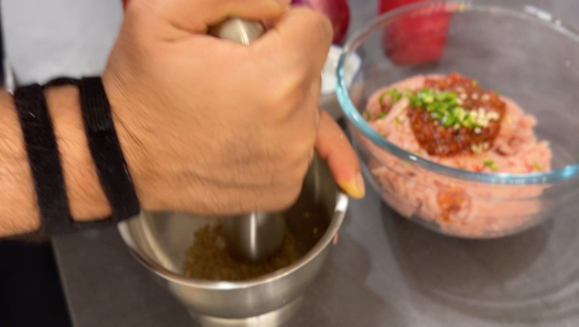 Hand pouring olive oil into a bowl of spicy Italian chicken sausage mixture with herbs.