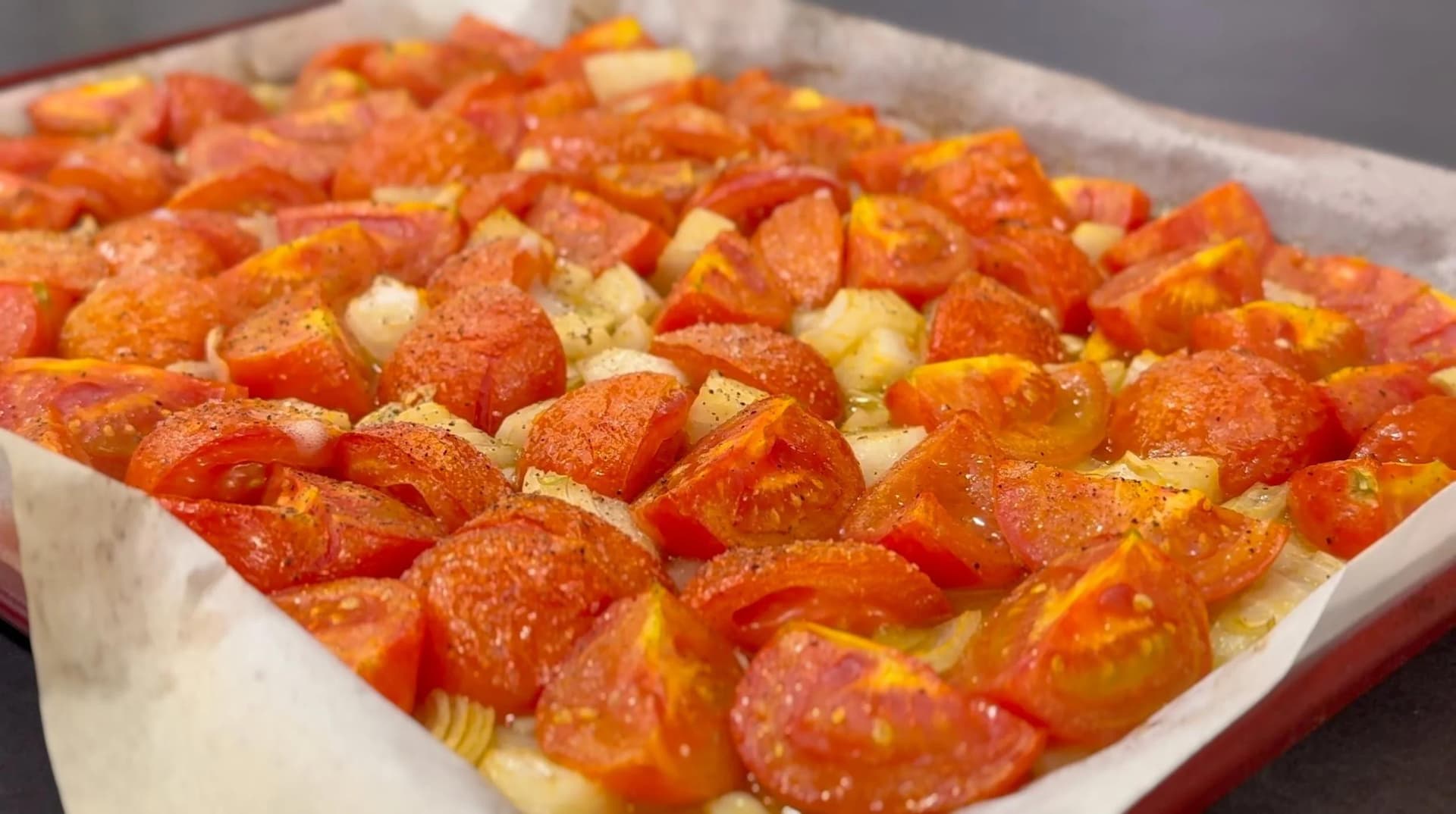 Tomatoes, onions, and garlic drizzled with olive oil on a parchment-lined baking sheet, ready to roast.