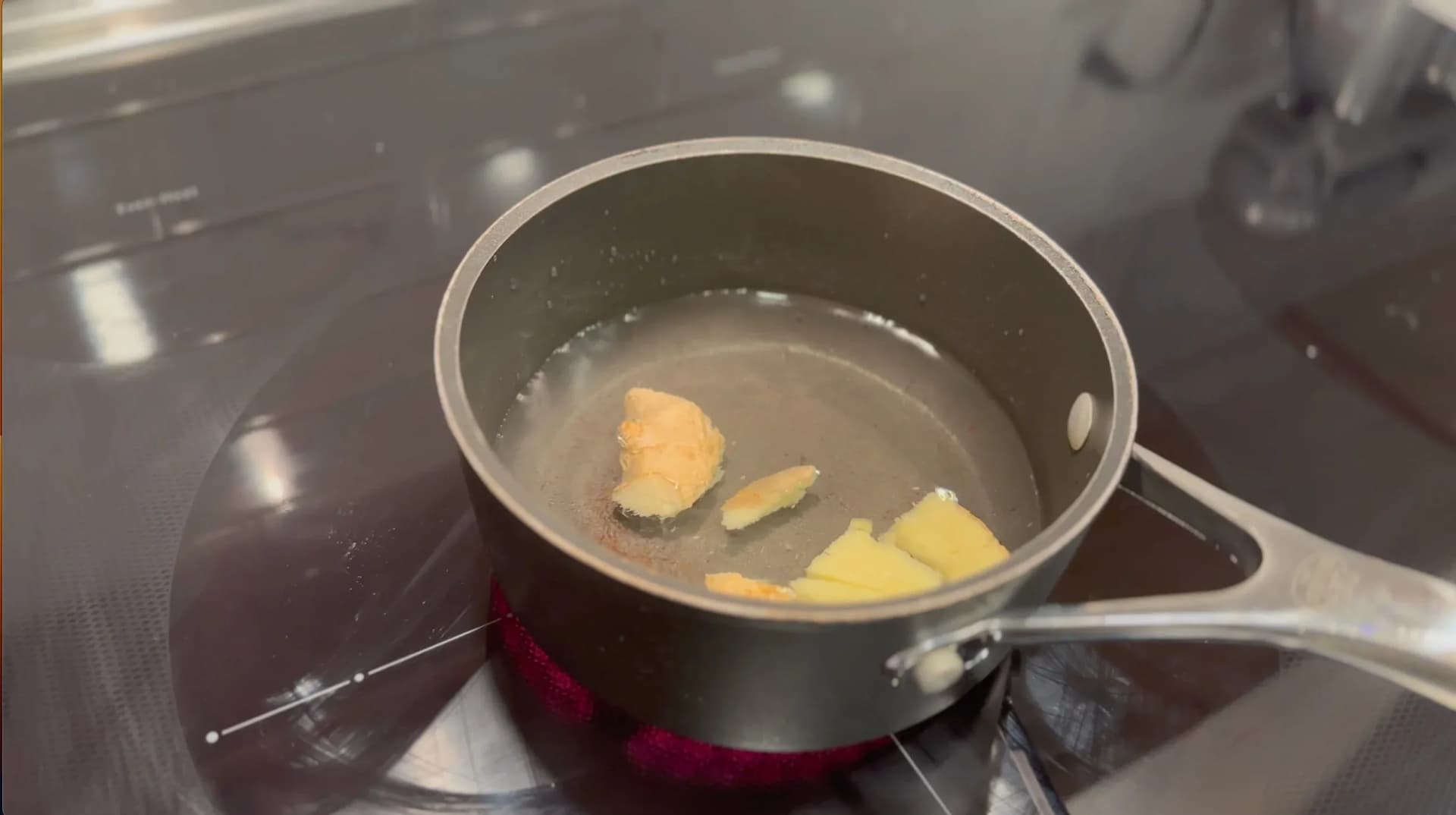 Saucepan with ginger pieces and spices simmering in water on a stovetop.