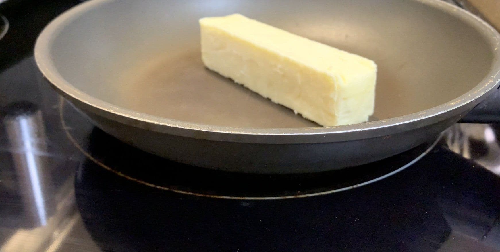 Stick of butter melting in a stainless steel pan on stovetop.