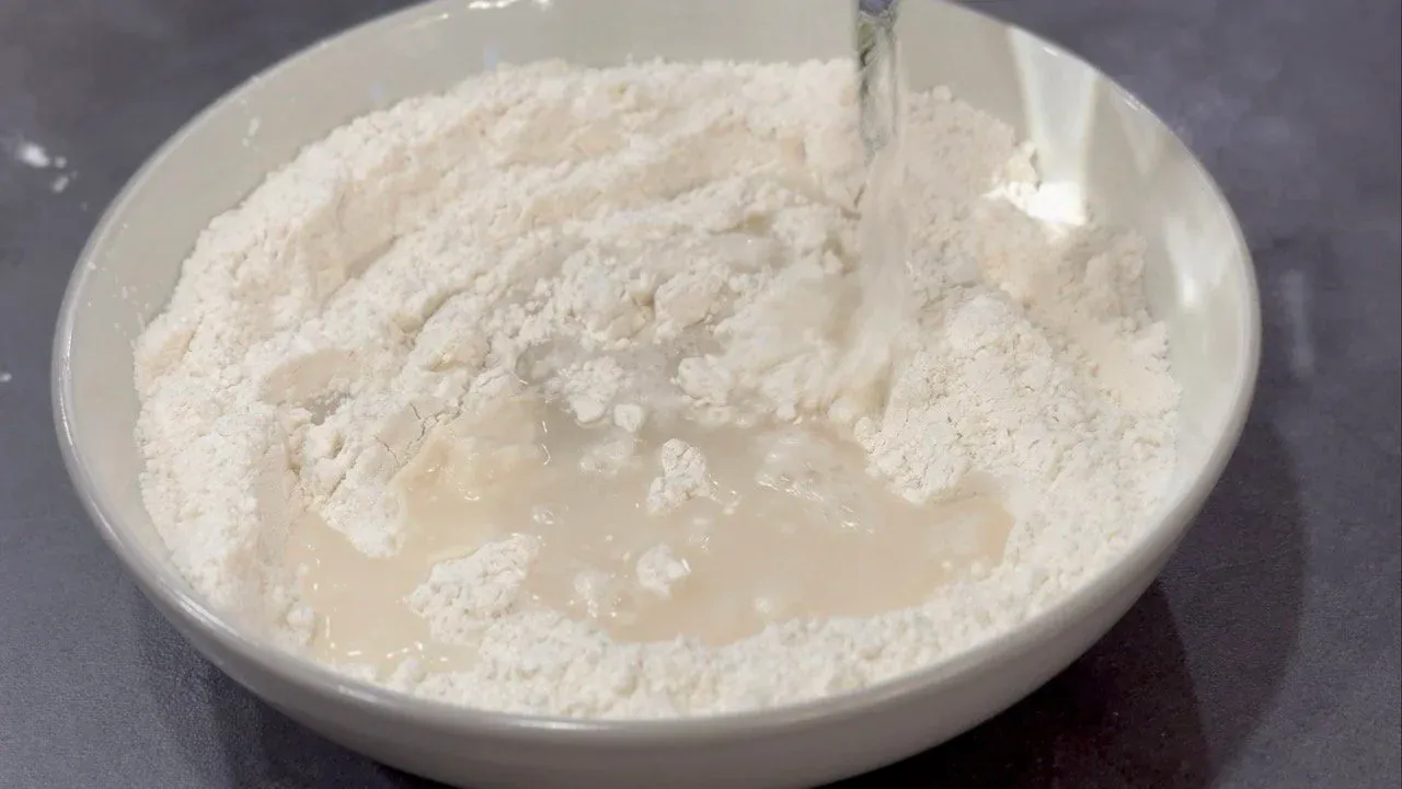 Flour and water combined in a white bowl during momo dough preparation.