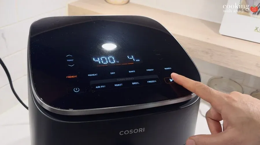Hand pointing to COSORI air fryer display showing 400°F temperature setting for cooking.