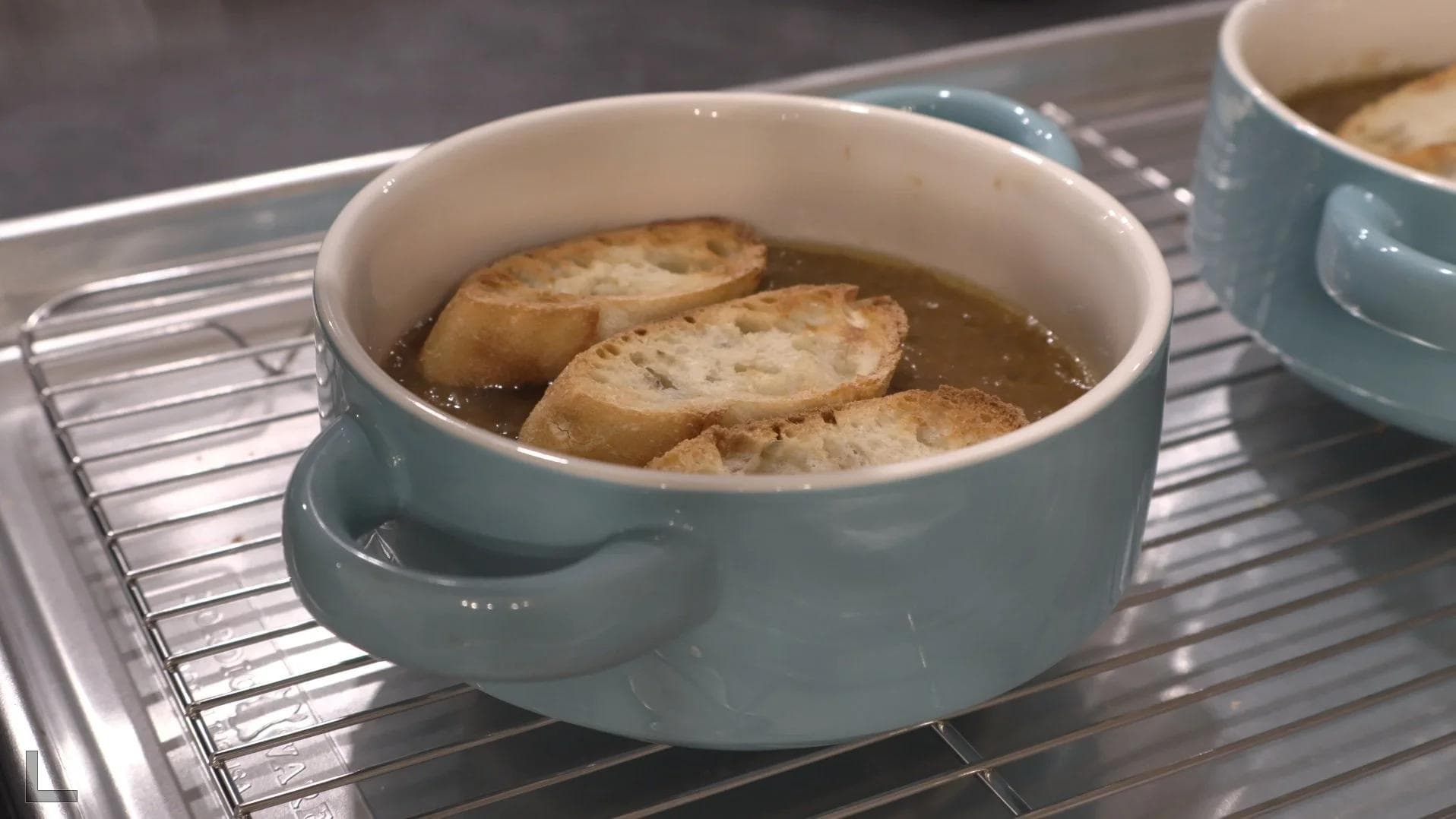 French onion soup in blue bowls with toasted baguette slices on top, ready for broiling.