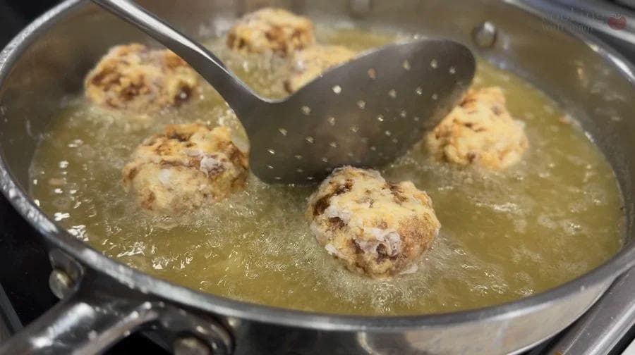 Golden-brown perkedel potato fritters frying in oil in a skillet with a slotted spatula.