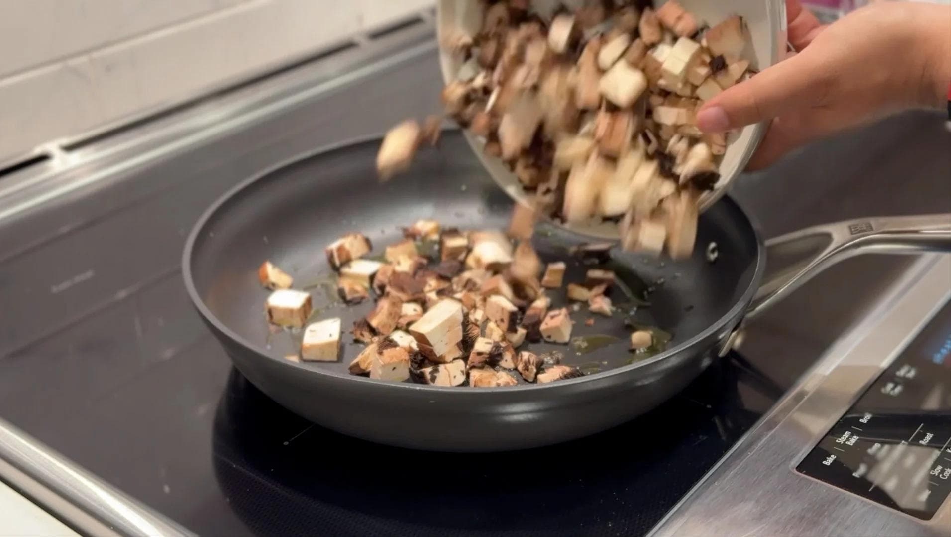 Diced mushrooms being poured into a dark skillet on a stovetop for sautéing.
