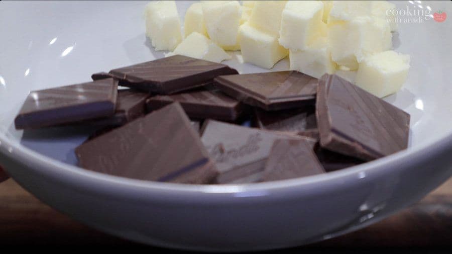 Chopped dark chocolate and diced white butter in a white bowl over simmering water for melting.