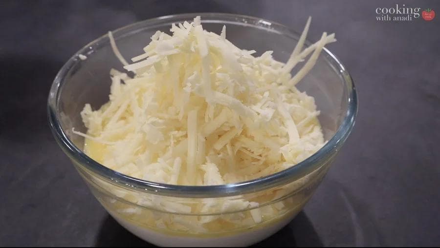 Shredded cheddar cheese mixed with cottage cheese and sour cream filling in a glass bowl.